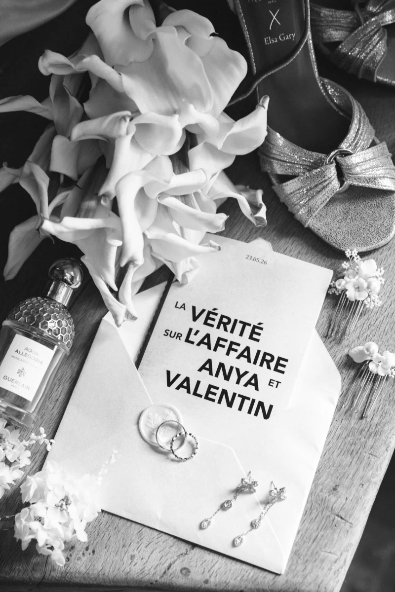 Flatlay en noir et blanc : faire-part, alliances, boucles d'oreilles, parfum, escarpins et arums
