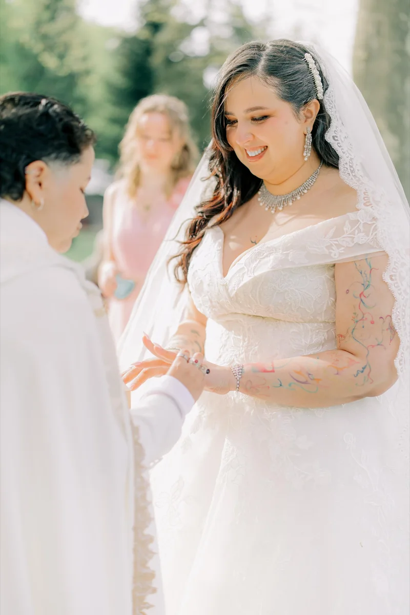 Échange des alliances : la mariée en voile de dentelle sourit pendant que sa partenaire lui passe la bague au doigt