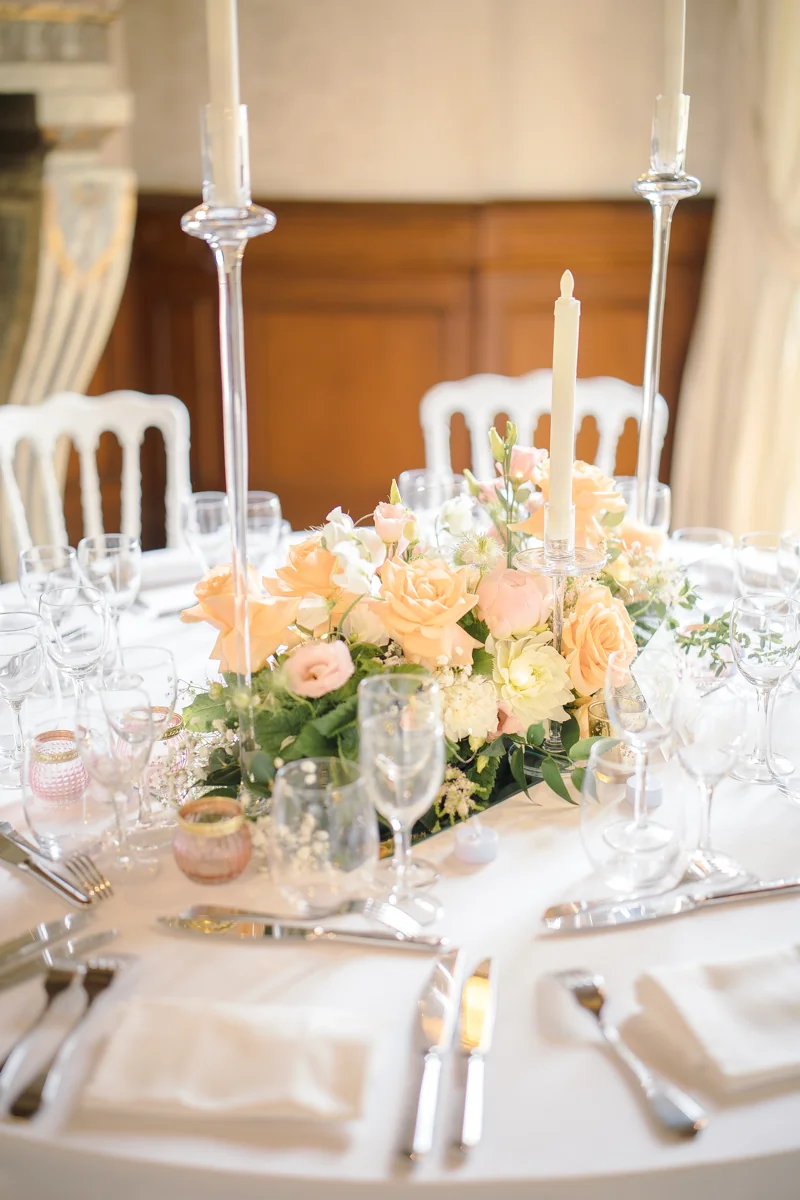 Table ronde de mariage avec couronne de roses pêche et blanches, bougies sur hauts chandeliers en verre